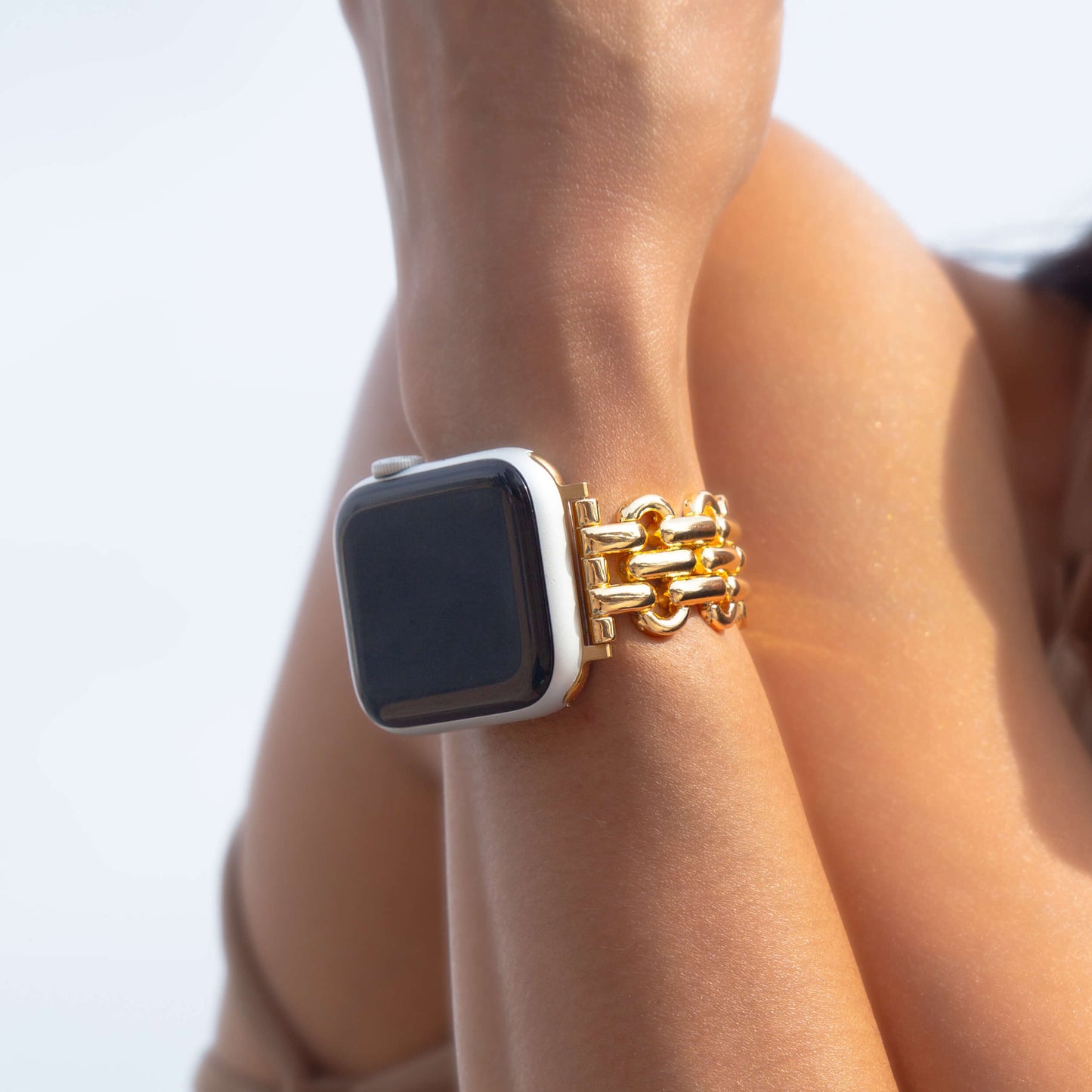 Gold chain link Apple Watch band worn on a wrist against a bright white background. Metal iWatch bracelet that complements every outfit, compatible with Apple Watch 38mm to 49mm, Series 1-11, SE and Ultra