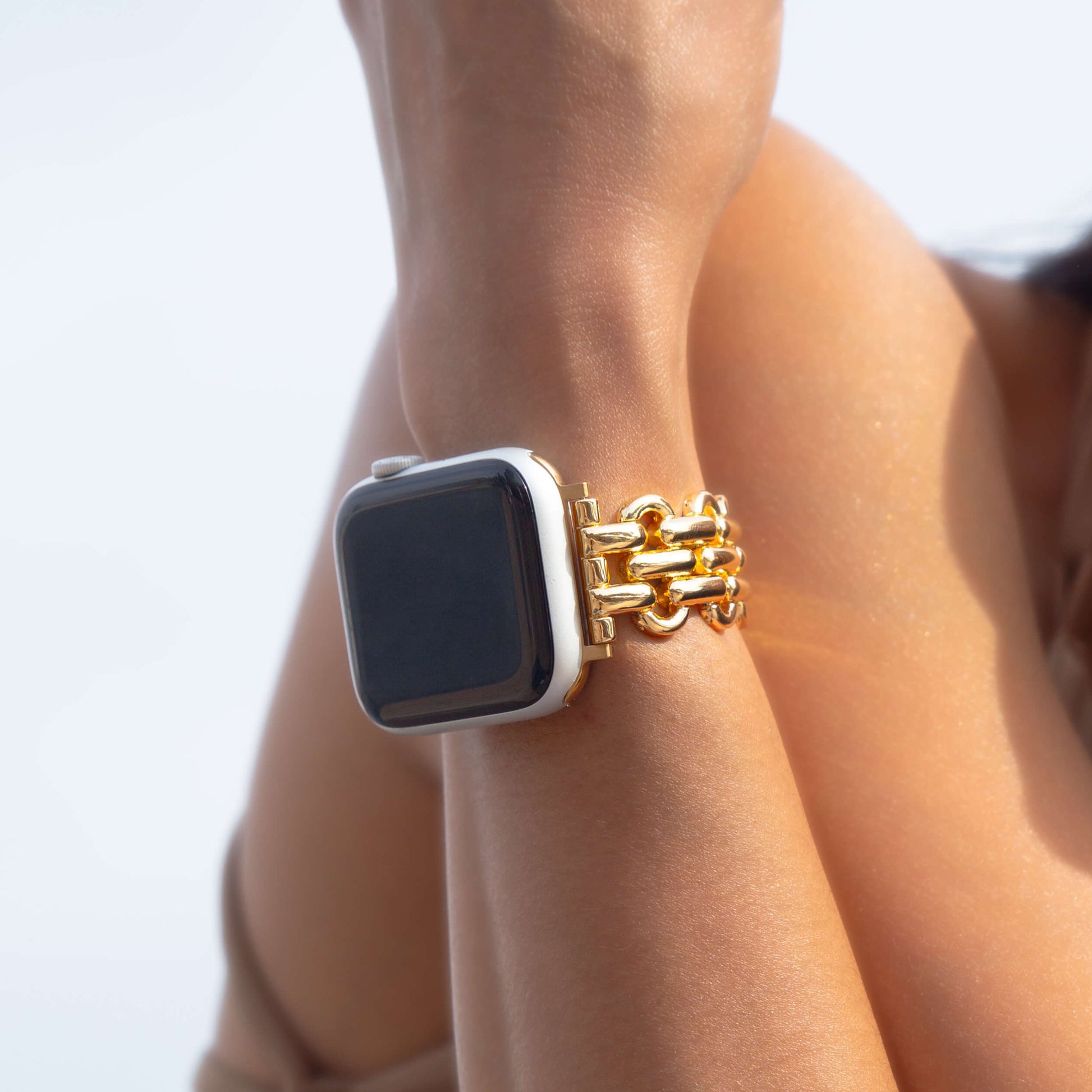 Gold chain link Apple Watch band worn on a wrist against a bright white background. Metal iWatch bracelet that complements every outfit, compatible with Apple Watch 38mm to 49mm, Series 1-11, SE and Ultra