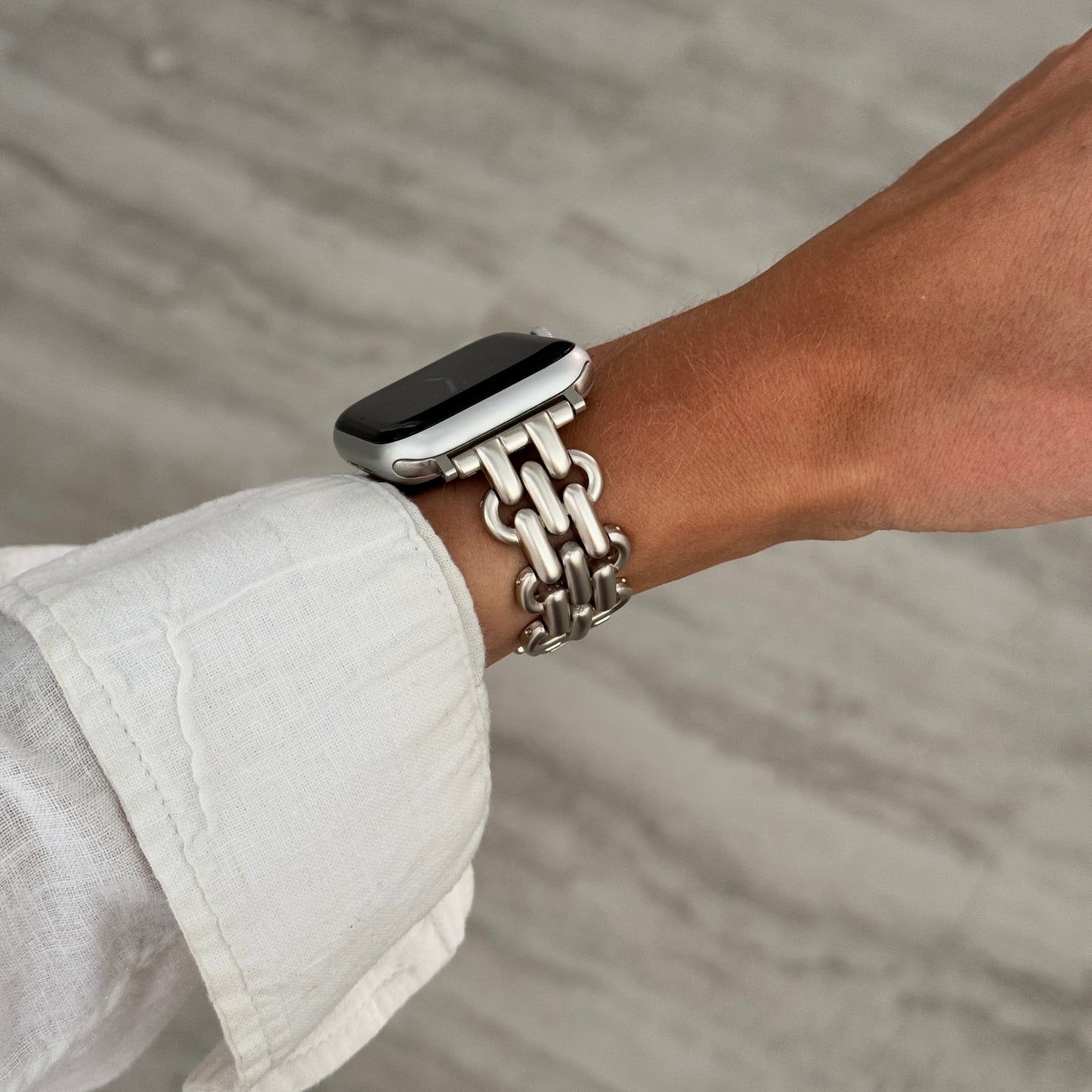 Starlight chain link Apple Watch band worn on a wrist with a white linen sleeve. Fashionable metal iWatch bracelet, compatible with Apple Watch 38mm to 49mm, Series 1-11, SE and Ultra