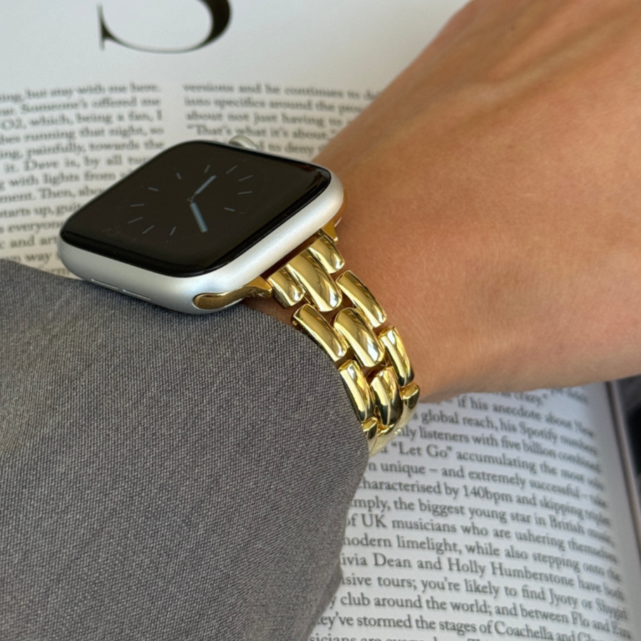 Gold slim link Apple Watch band worn on a wrist above an open book, metal bracelet for Apple Watch 38mm to 49mm