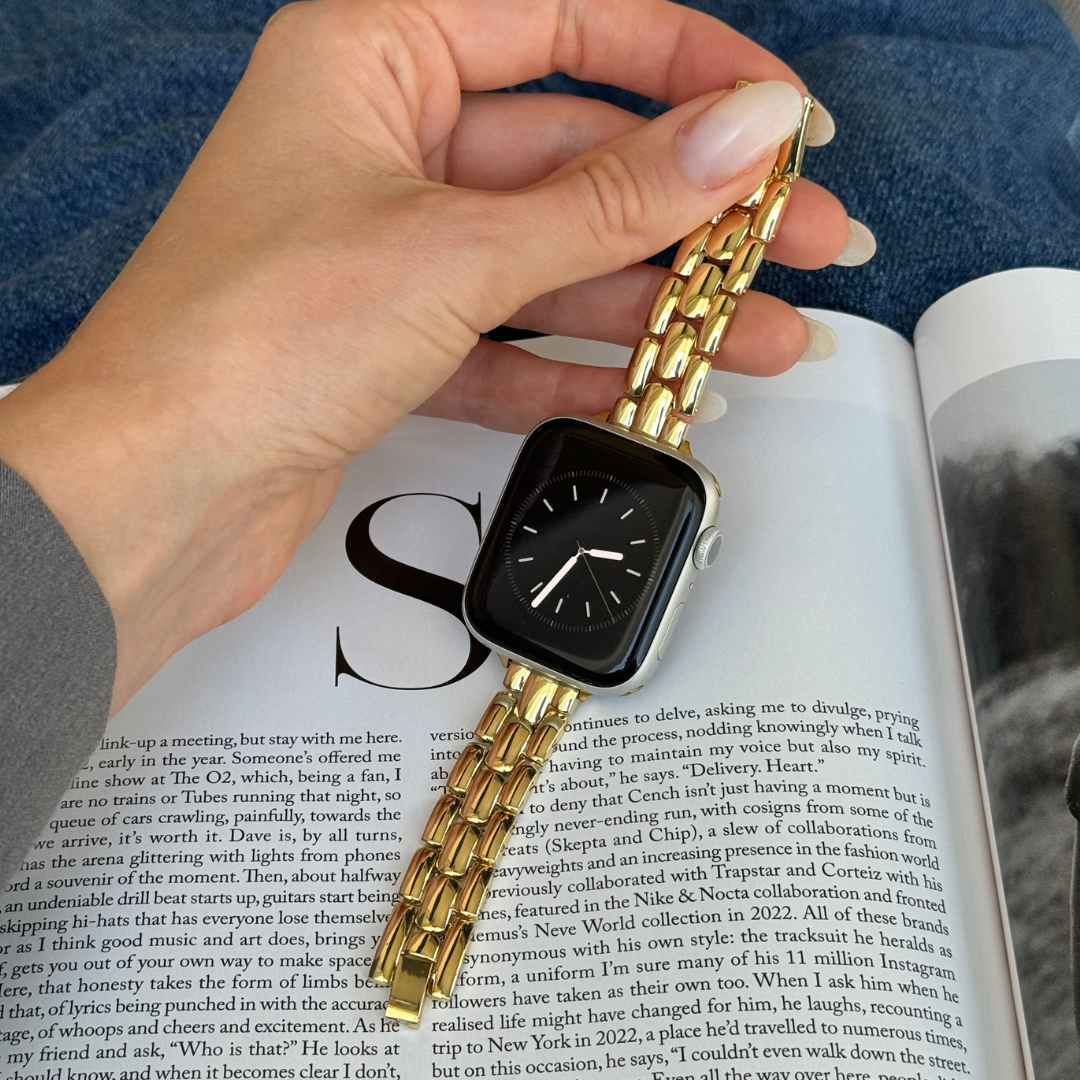 Gold slim link Apple Watch band held in a hand over an open magazine, metal strap for Apple Watch 38mm to 49mm