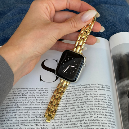 Gold slim link Apple Watch band held in a hand over an open magazine, metal strap for Apple Watch 38mm to 49mm