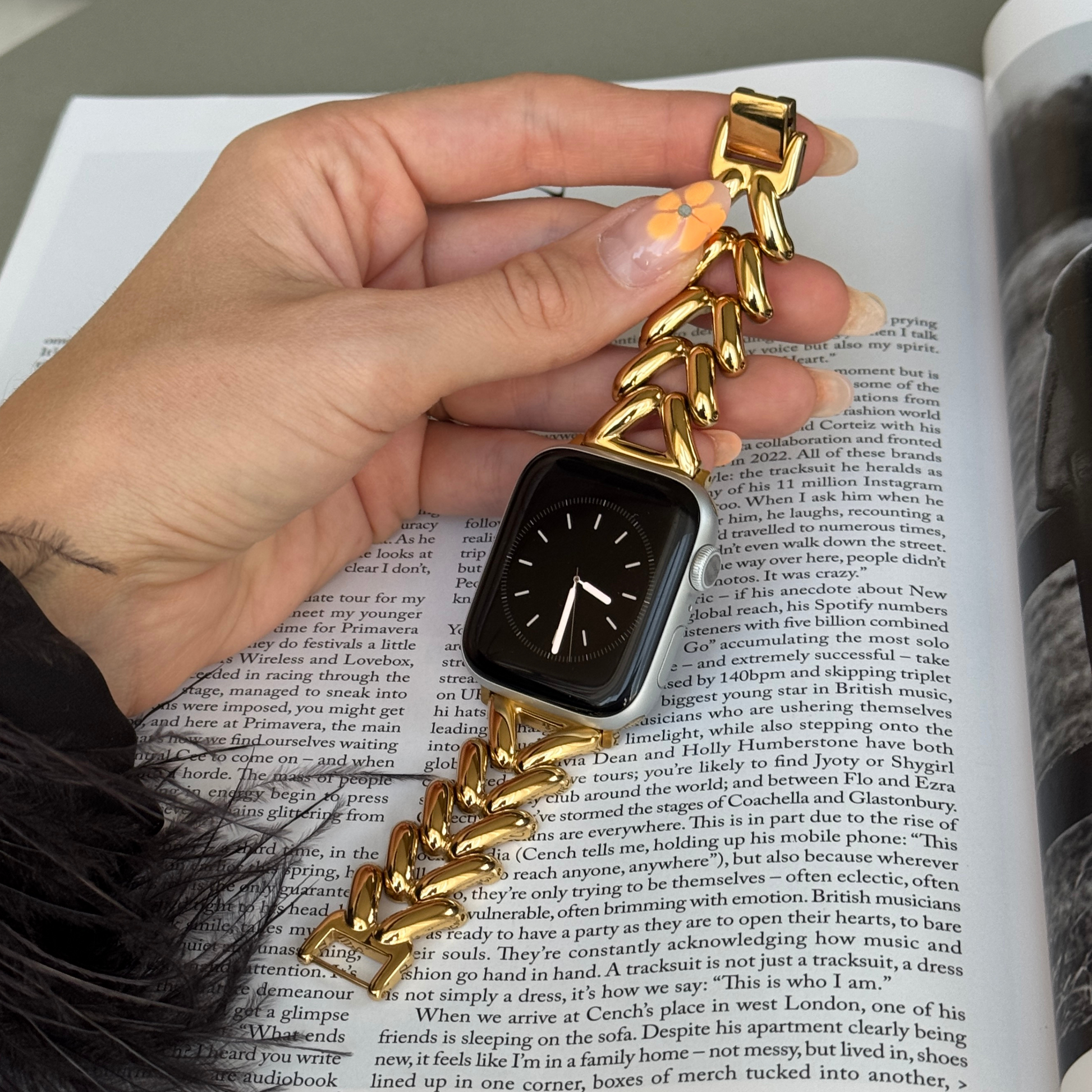 Gold chunky chain Apple Watch band held in a hand over an open book. Feminine metal iWatch strap, compatible with Apple Watch 38mm to 49mm, Series 1-11, SE and Ultra