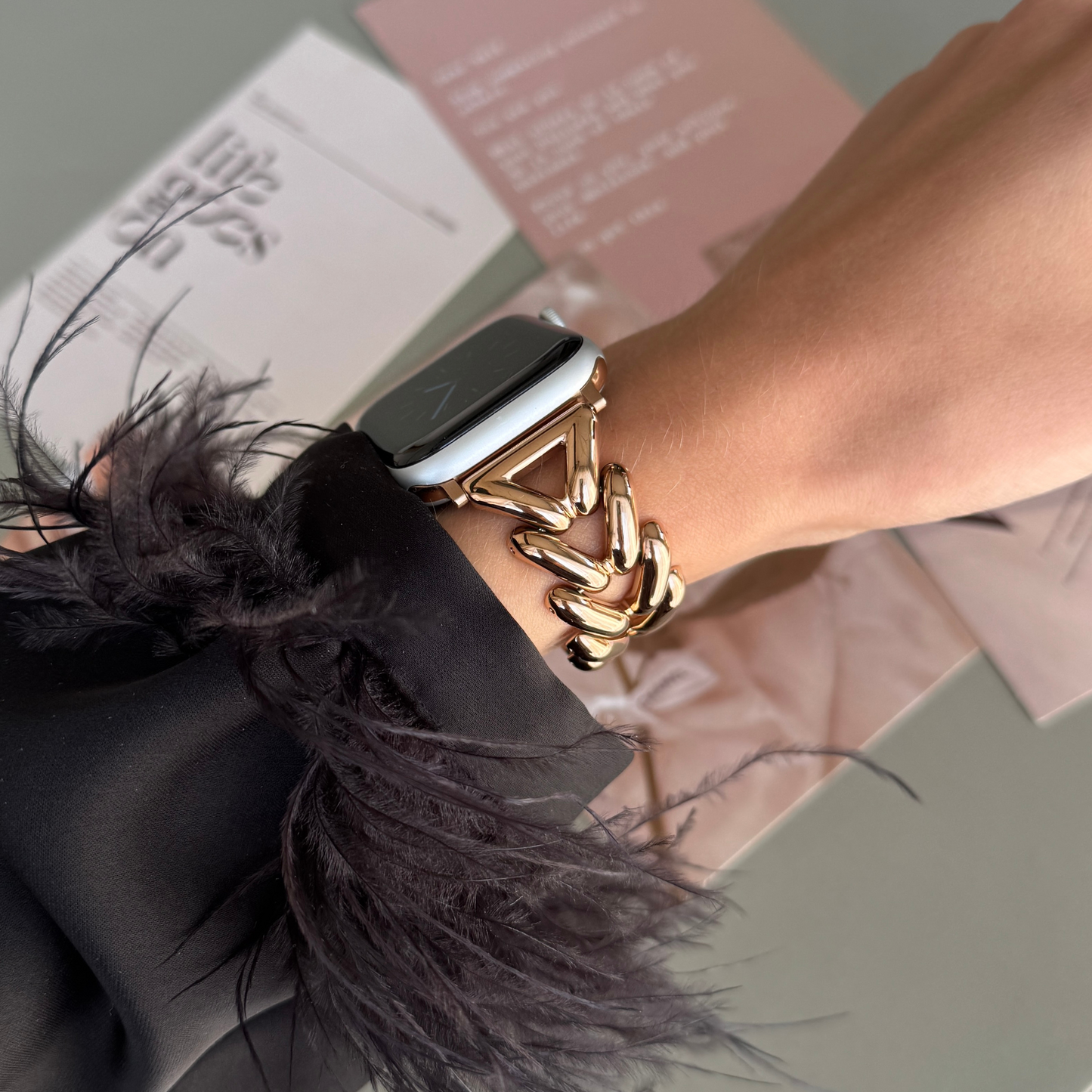 Rose gold chunky chain Apple Watch band worn on a wrist above pink paper cards. Feminine metal iWatch bracelet, compatible with Apple Watch 38mm to 49mm, Series 1-11, SE and Ultra