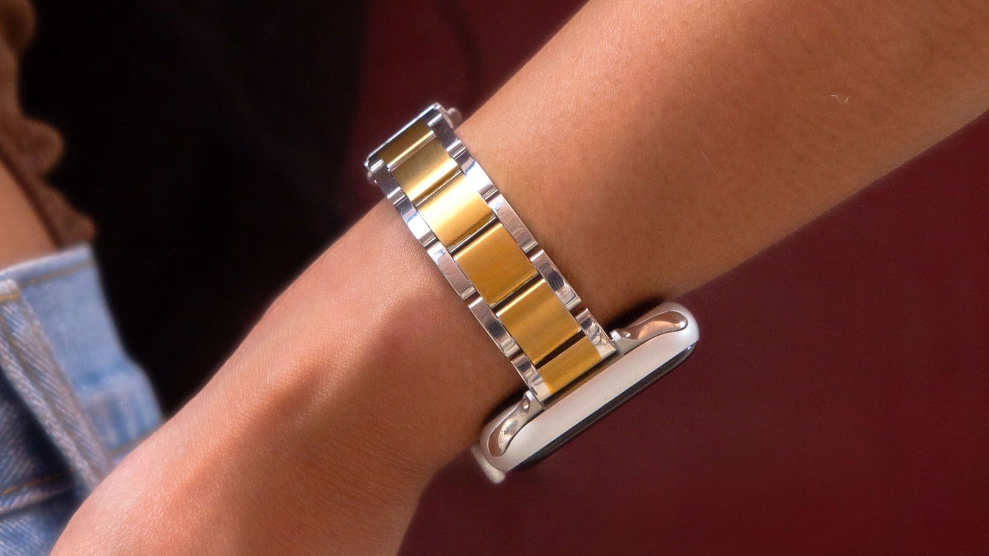 Silver gold slim link Apple Watch band shown close up on a wrist beside denim, stainless steel bracelet for Apple Watch 38mm to 49mm