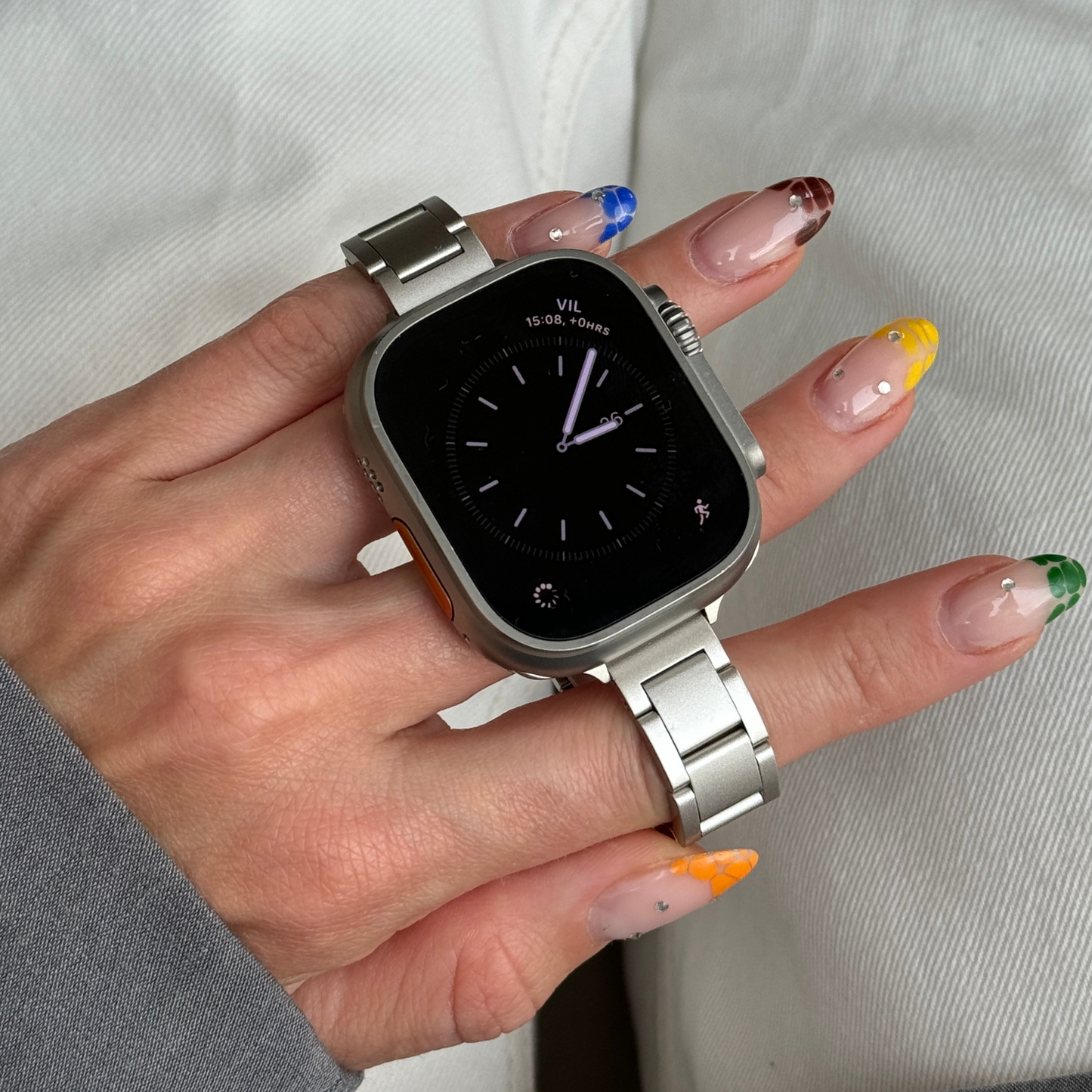Starlight slim link Apple Watch band held in a hand with brightly painted nails, stainless steel bracelet for Apple Watch 38mm to 49mm