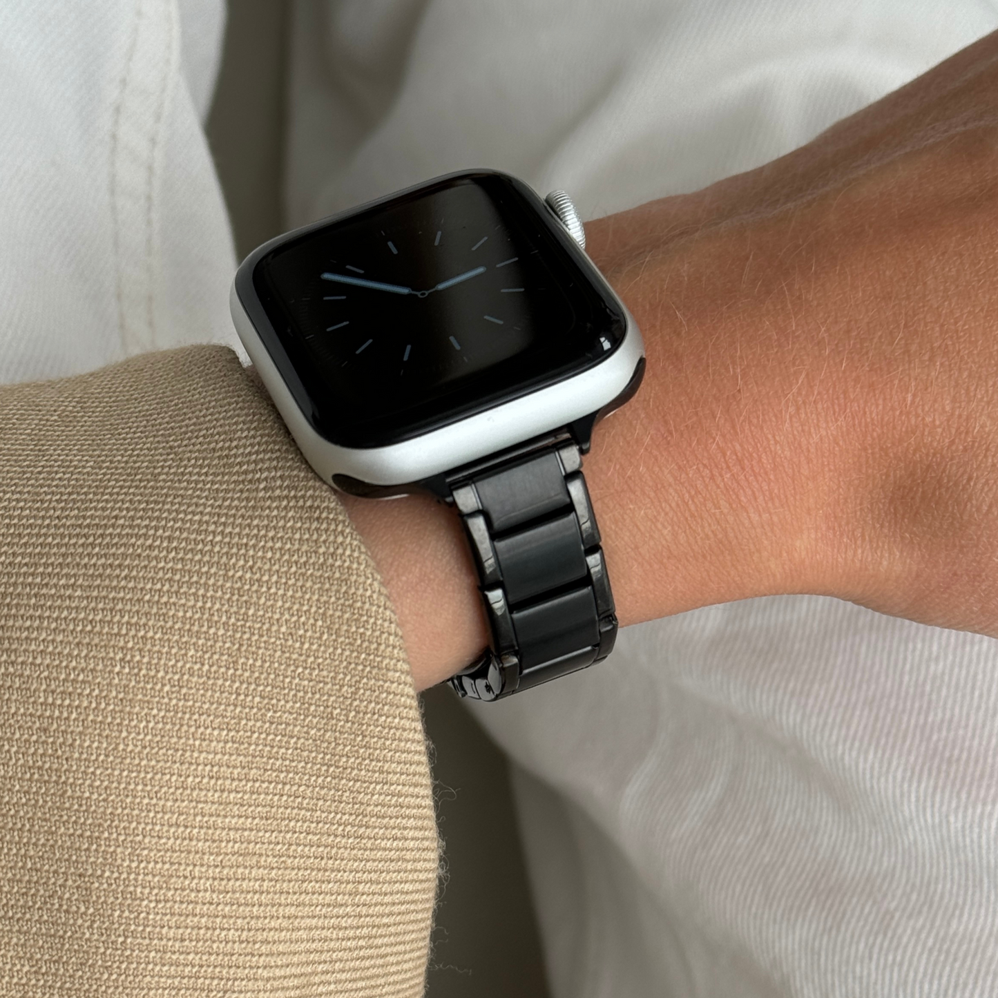 Black slim link Apple Watch band worn with a camel sleeve against cream fabric, stainless steel bracelet for Apple Watch 38mm to 49mm