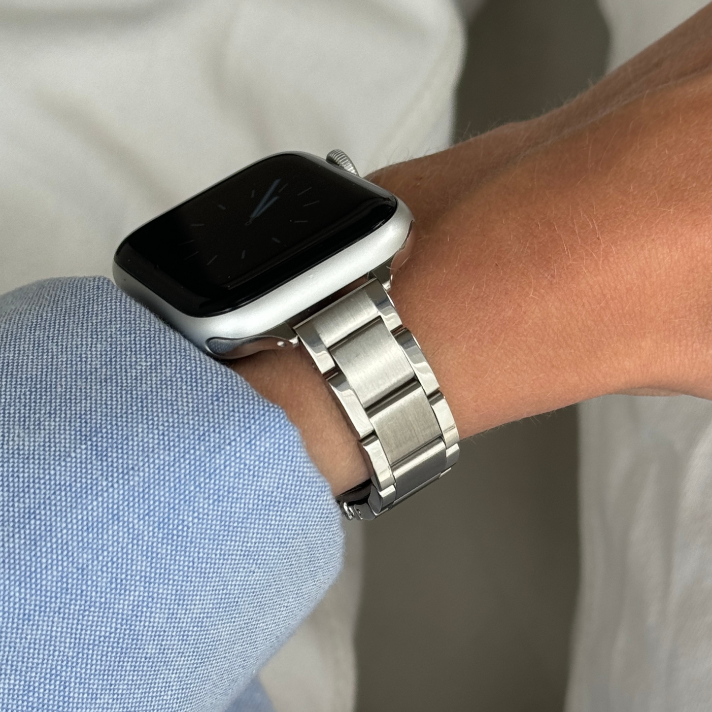 Silver slim link Apple Watch band worn on a wrist with a blue shirt cuff, stainless steel strap for Apple Watch 38mm to 49mm