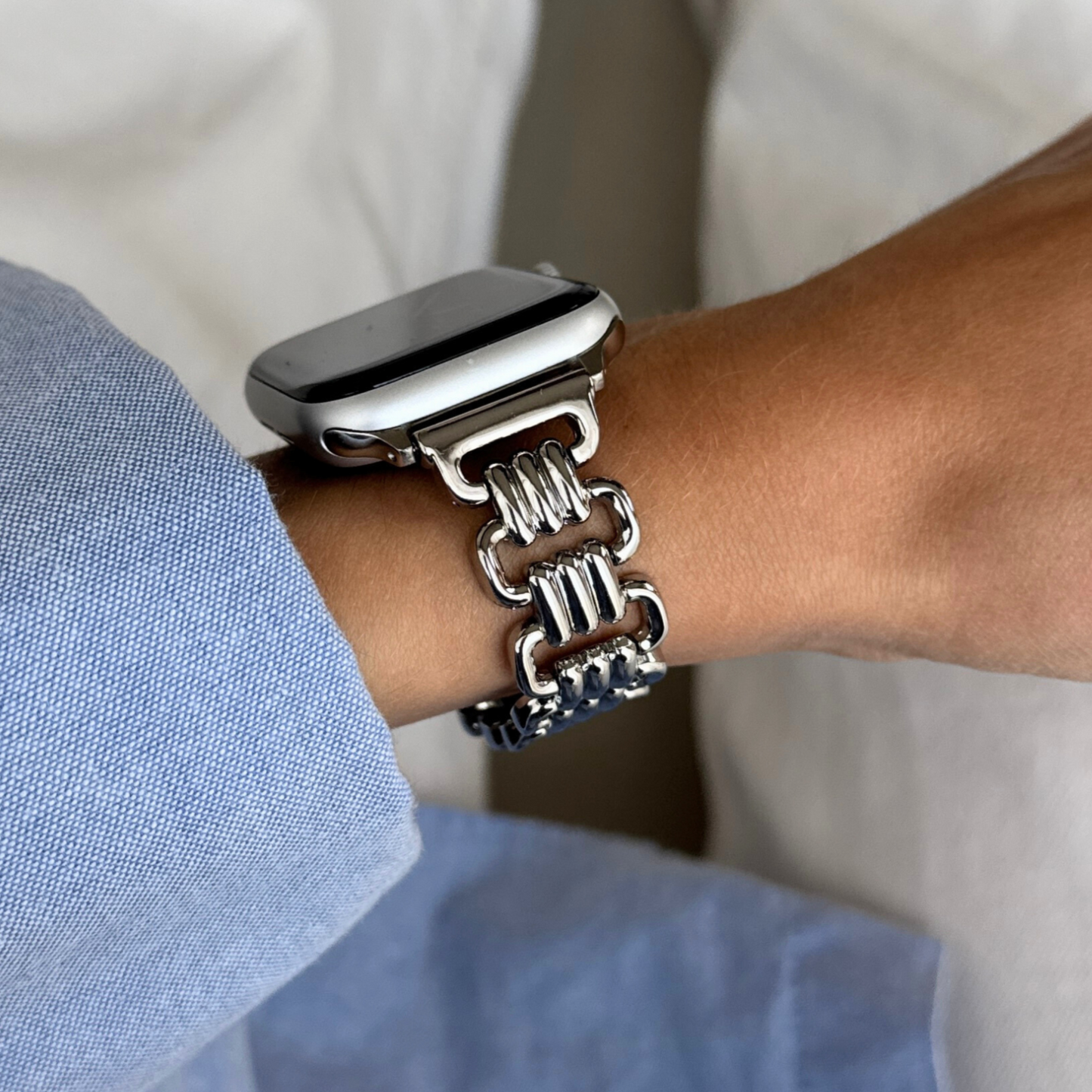 Silver open link Apple Watch band worn on a wrist with a blue shirt cuff. Luxurious metal iWatch strap for women, compatible with Apple Watch 38mm to 49mm, Series 1-11, SE and Ultra