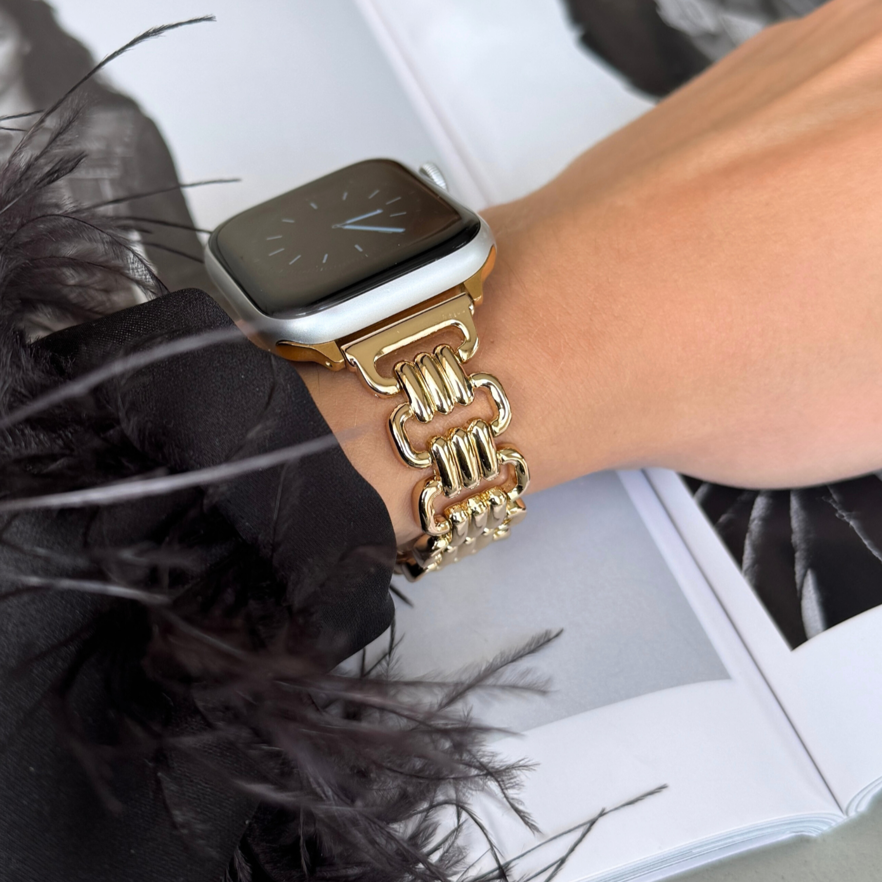 Gold open link Apple Watch band worn on a wrist with a feather trimmed cuff. Statement metal iWatch bracelet, compatible with Apple Watch 38mm to 49mm, Series 1-11, SE and Ultra
