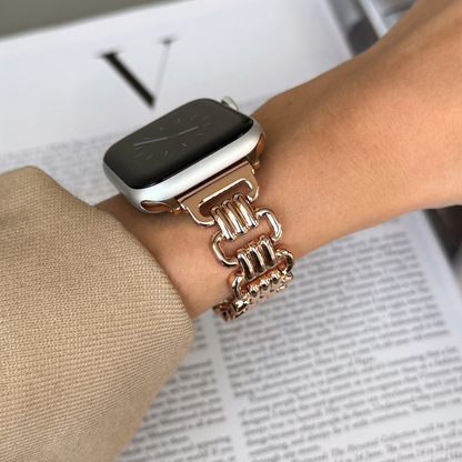 Rose gold open link Apple Watch band worn with a camel sleeve above an open book. Elegant metal iWatch armband, compatible with Apple Watch 38mm to 49mm, Series 1-11, SE and Ultra