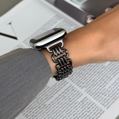 Black open link Apple Watch band worn with a grey sleeve over a newspaper. High-end metal iWatch strap, compatible with Apple Watch 38mm to 49mm, Series 1-11, SE and Ultra