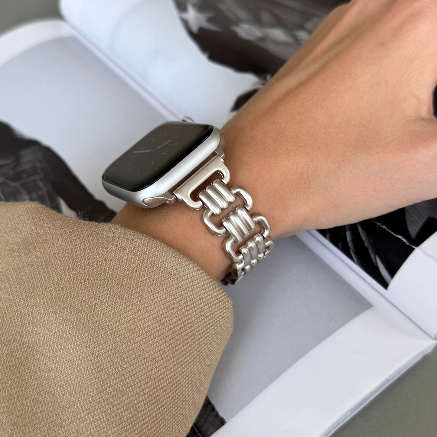 Starlight open link Apple Watch band worn with a camel sleeve beside a magazine. Unique metal iWatch bracelet for women, compatible with Apple Watch 38mm to 49mm, Series 1-11, SE and Ultra