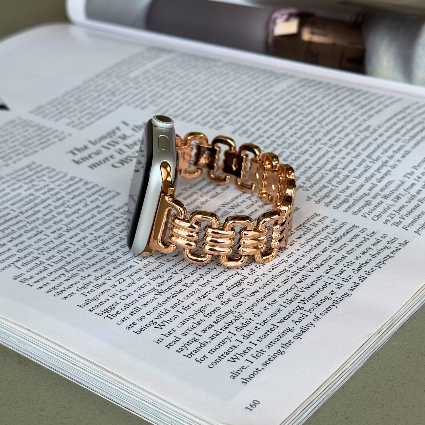 Rose gold open link Apple Watch band lying flat on an open magazine. Feminine metal iWatch strap, compatible with Apple Watch 38mm to 49mm, Series 1-11, SE and Ultra