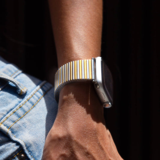 Silver gold ribbed loop Apple Watch band worn on a wrist over denim in bright sunlight. Waterproof stainless steel iWatch bracelet, compatible with Apple Watch 38mm, 40mm, 41mm, 42mm, 44mm, 45mm, 46mm and 49mm, Series 1-11, SE and Ultra