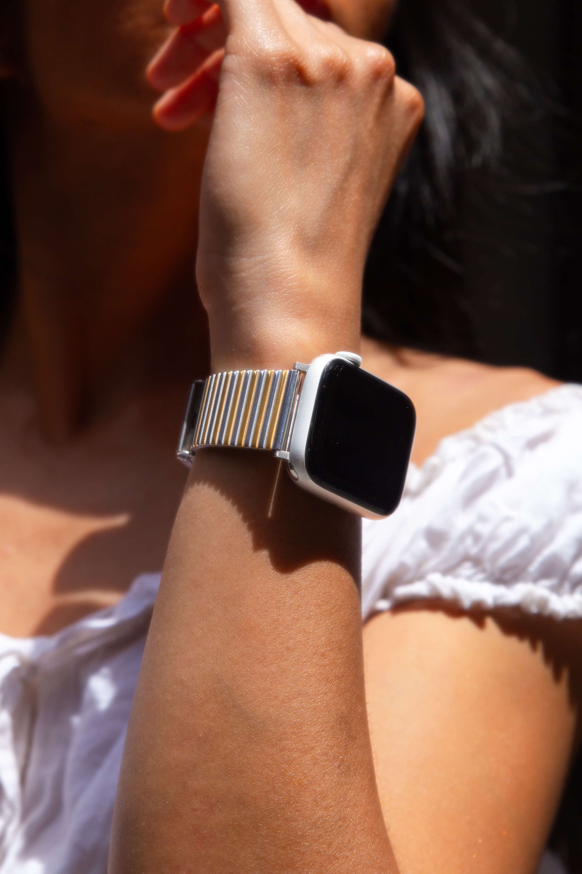 Silver gold ribbed loop Apple Watch band worn outdoors with a white blouse. Chic stainless steel iWatch armband, compatible with Apple Watch 38mm to 49mm, Series 1-11, SE and Ultra