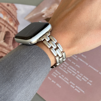 Starlight slim link Apple Watch band worn on a wrist beside a travel poster, metal strap for Apple Watch 38mm to 49mm