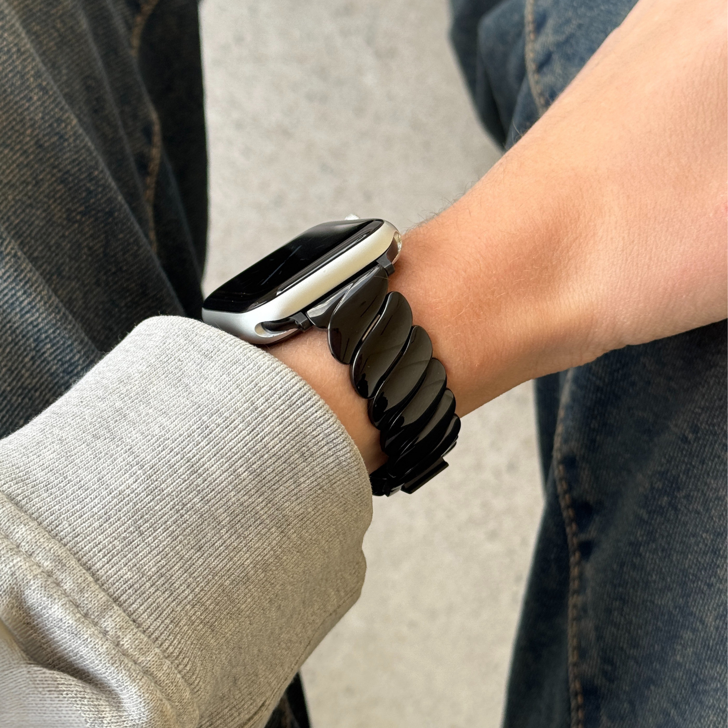 Black twisted link Apple Watch band worn with a grey sleeve over denim. Bold statement stainless steel iWatch strap, compatible with Apple Watch 38mm to 49mm, Series 1-11, SE and Ultra