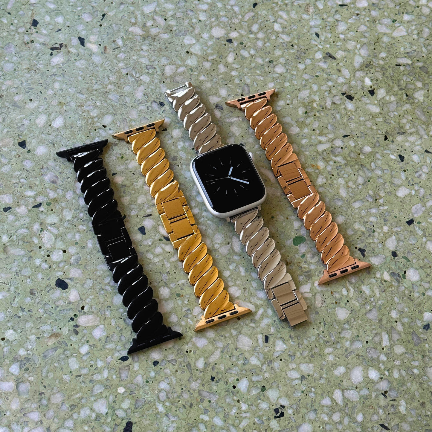 Black, gold, silver and rose gold twisted link Apple Watch bands laid out on terrazzo. Waterproof stainless steel iWatch straps, compatible with Apple Watch 38mm to 49mm, Series 1-11, SE and Ultra