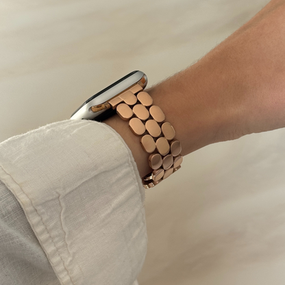 Rose gold pebble link Apple Watch band worn on a wrist with a cream linen sleeve. Elegant stainless steel iWatch strap, compatible with Apple Watch 38mm to 49mm, Series 1-11, SE and Ultra