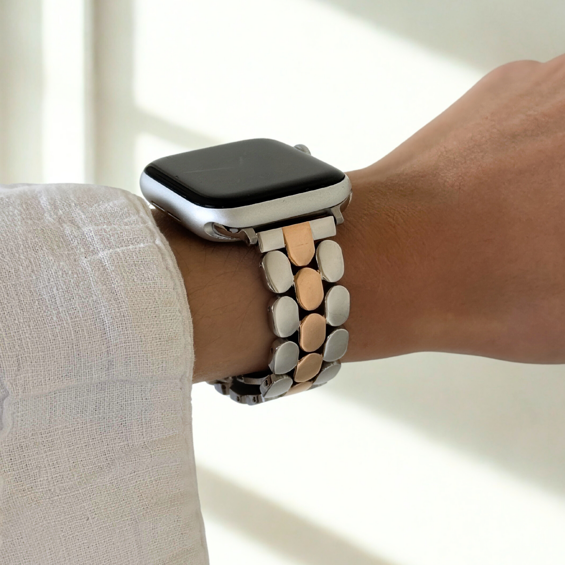 Silver rose gold pebble link Apple Watch band worn on a wrist with a white linen sleeve. Elegant stainless steel iWatch bracelet with a butterfly clasp, compatible with Apple Watch 38mm to 49mm, Series 1-11, SE and Ultra