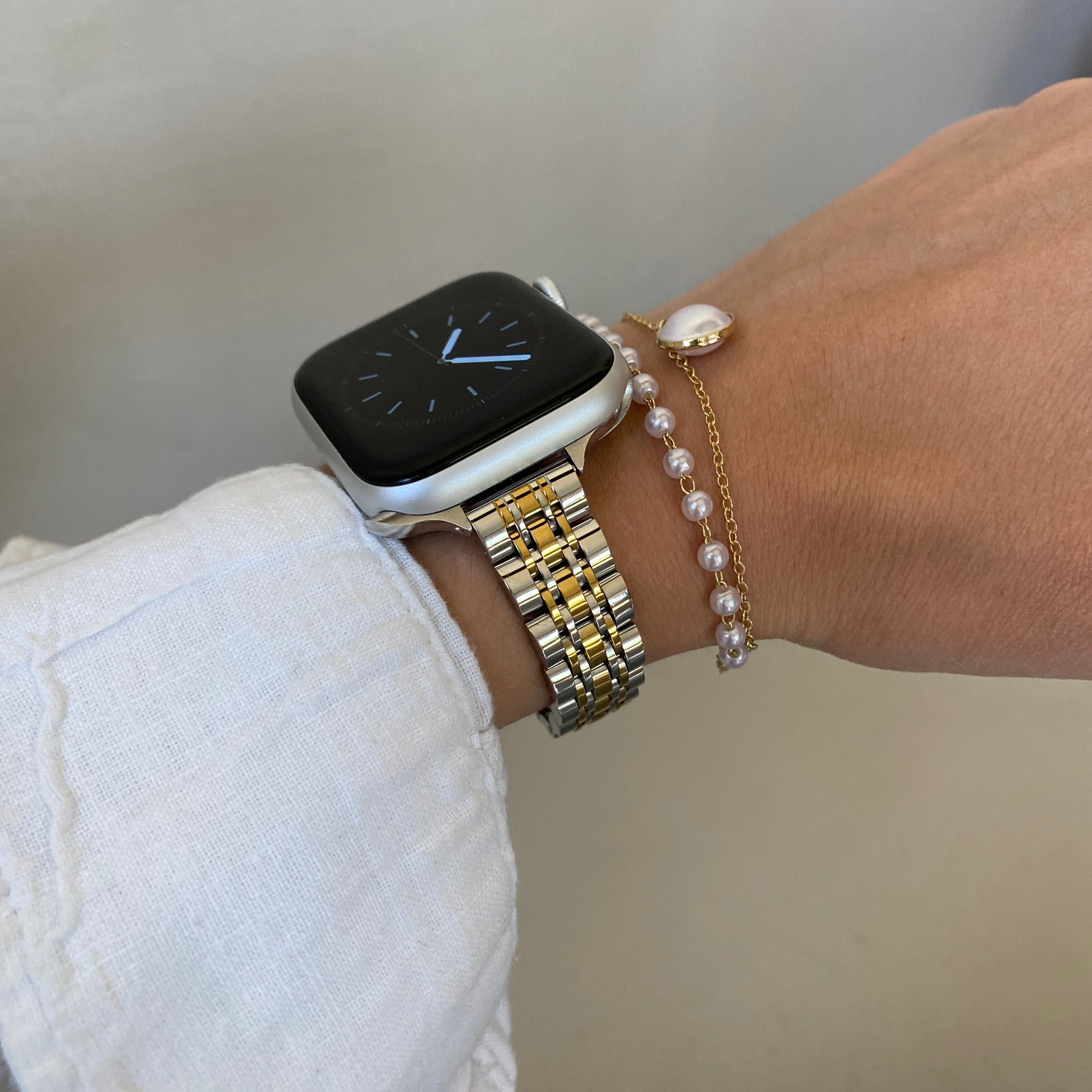 Silver gold woven link Apple Watch band worn on a wrist beside a pearl bracelet, stainless steel bracelet for Apple Watch 38mm to 49mm