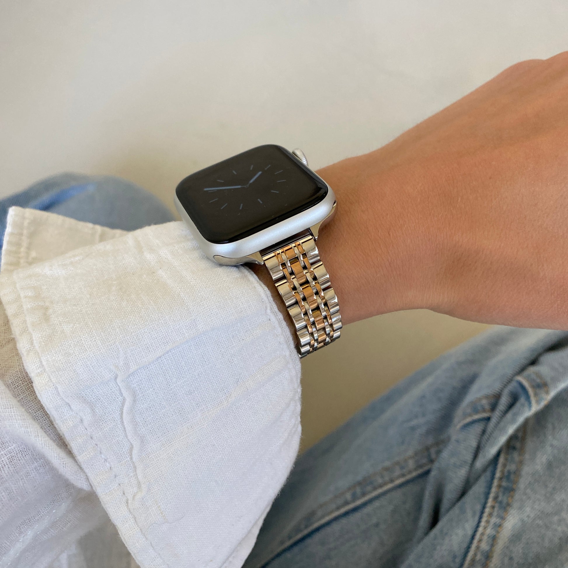 Silver rose gold woven link Apple Watch band worn with a white linen cuff over denim, stainless steel bracelet for Apple Watch 38mm to 49mm