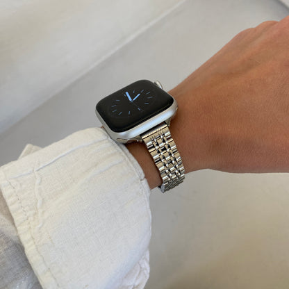 Silver woven link Apple Watch band worn with a white linen cuff against a pale wall, stainless steel strap for Apple Watch 38mm to 49mm