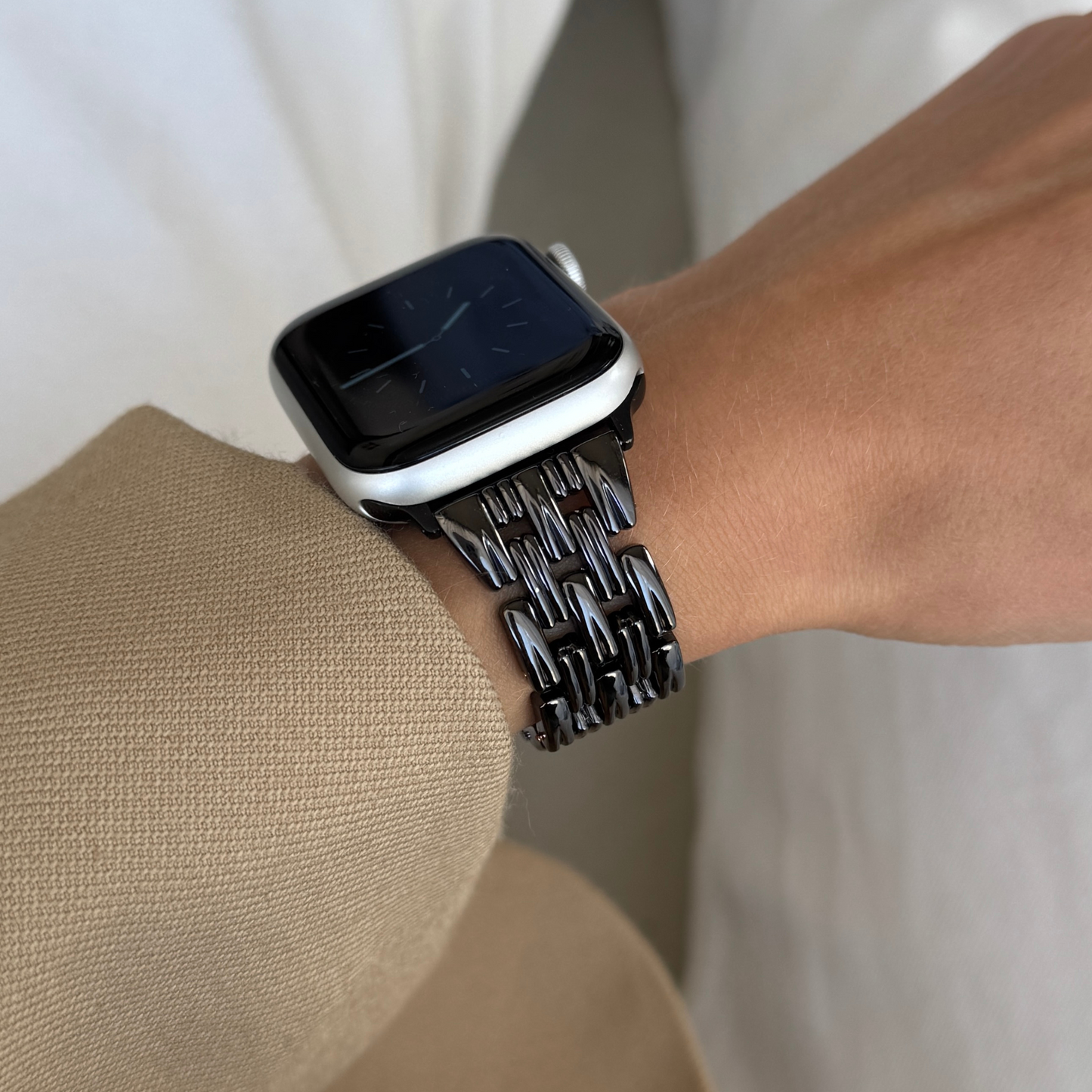 Black link Apple Watch band worn on a wrist with a beige sleeve. Sleek metal iWatch bracelet with a smooth interior, compatible with Apple Watch 38mm to 49mm, Series 1-11, SE and Ultra