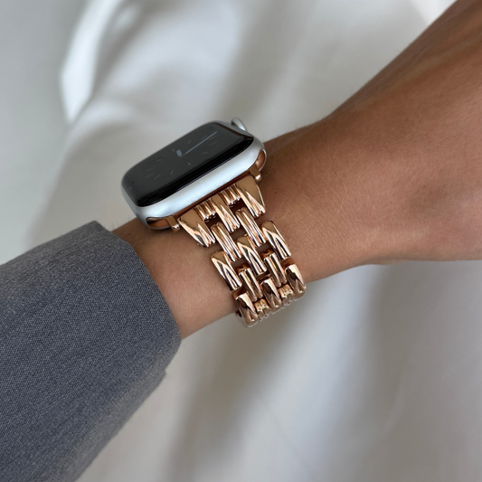 Rose gold link Apple Watch band worn on a wrist with a grey sleeve. Feminine metal iWatch bracelet with a smooth interior, compatible with Apple Watch 38mm, 40mm, 41mm, 42mm, 44mm, 45mm, 46mm and 49mm, Series 1-11, SE and Ultra