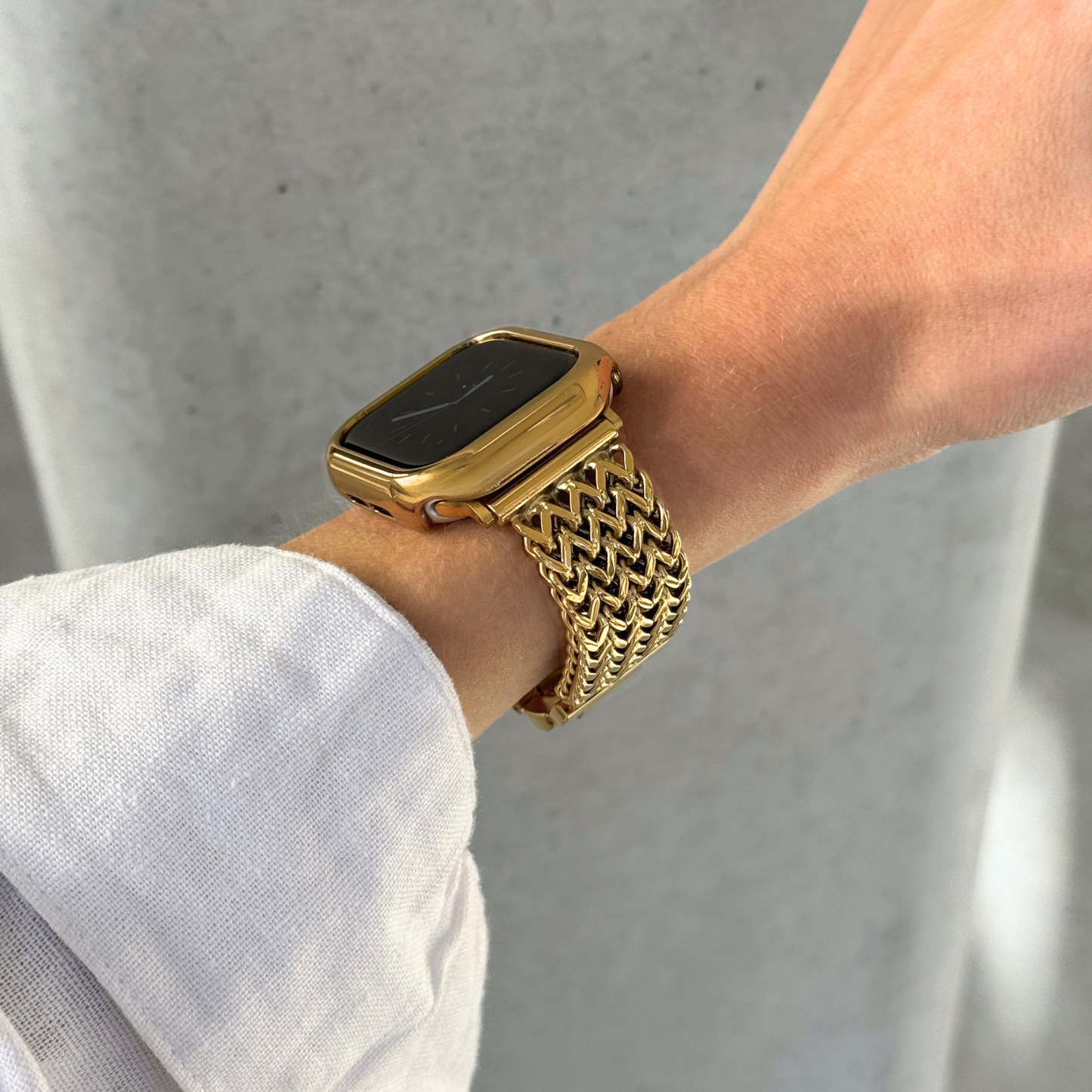 A close-up of a person's wrist wearing a gold toned Apple smartwatch with a woven mesh band and a matching gold bezel, set against a light background.