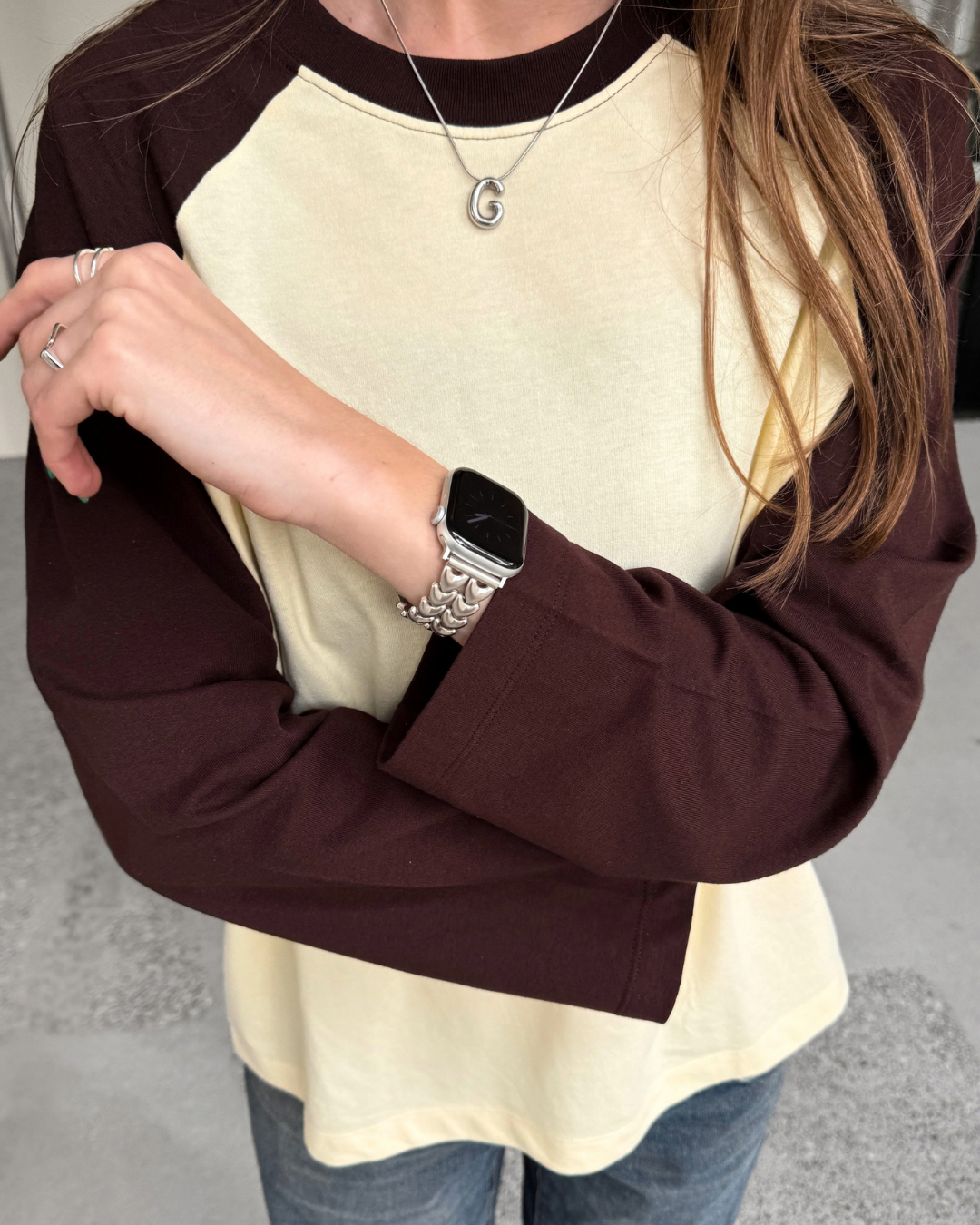A person wearing a long-sleeve raglan-style top with a yellow body and dark brown sleeves, paired with blue jeans. A person is wearing Apple Watch with a heart-shaped starlight colour Apple Watch Band