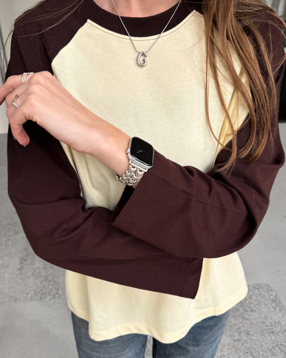 A person wearing a long-sleeve raglan-style top with a yellow body and dark brown sleeves, paired with blue jeans. A person is wearing Apple Watch with a heart-shaped starlight colour Apple Watch Band