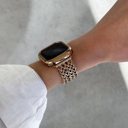 A close-up of a person's wrist wearing a rose gold toned Apple smartwatch with a matching metallic mesh band and bezel, set against a soft concrete background.