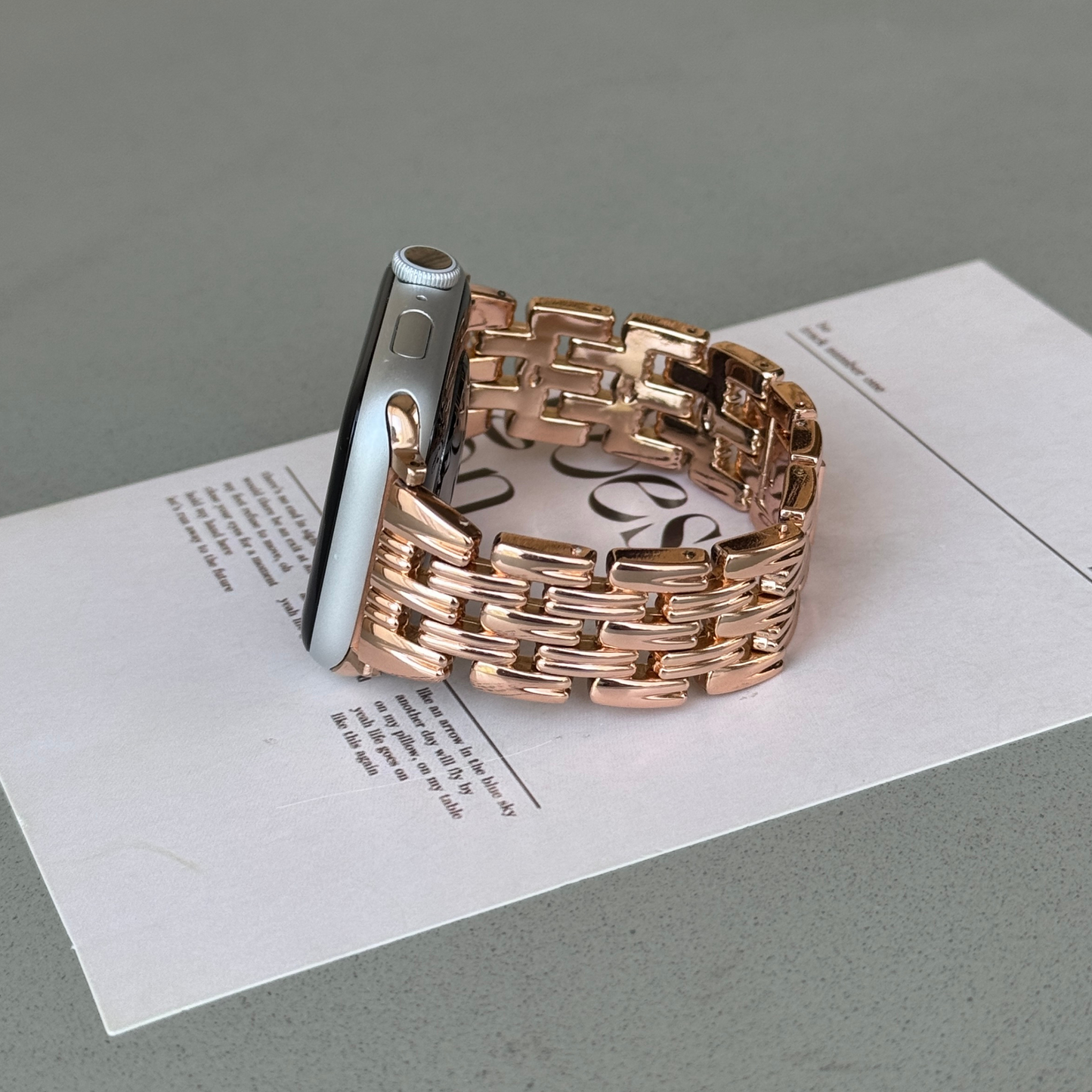 Rose gold link Apple Watch band propped upright on a printed card. Fashion forward metal iWatch armband, compatible with Apple Watch 38mm to 49mm, Series 1-11, SE and Ultra