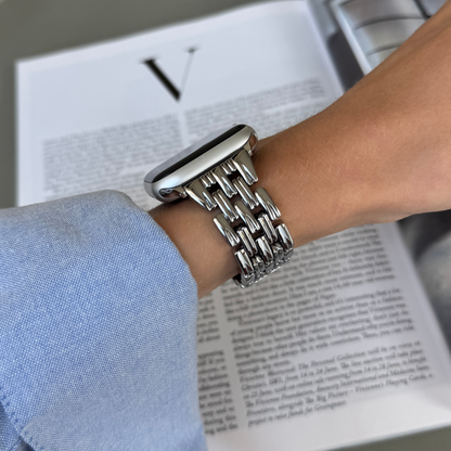 Silver link Apple Watch band worn on a wrist beside a fashion magazine. Metal iWatch bracelet with a smooth interior, compatible with Apple Watch 38mm to 49mm, Series 1-11, SE and Ultra