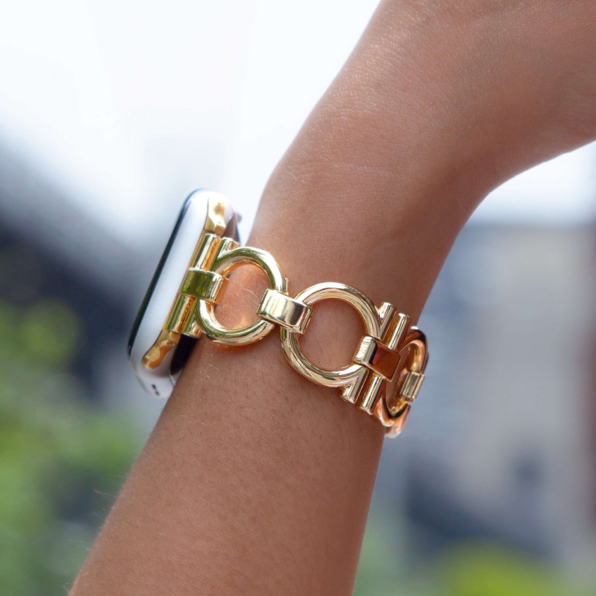 Gold circle link Apple Watch band worn on a wrist outdoors. Slim lightweight metal iWatch bracelet, easily resizable with no tools needed, compatible with Apple Watch 38mm, 40mm, 41mm, 42mm, 44mm, 45mm, 46mm and 49mm, Series 1-11, SE and Ultra