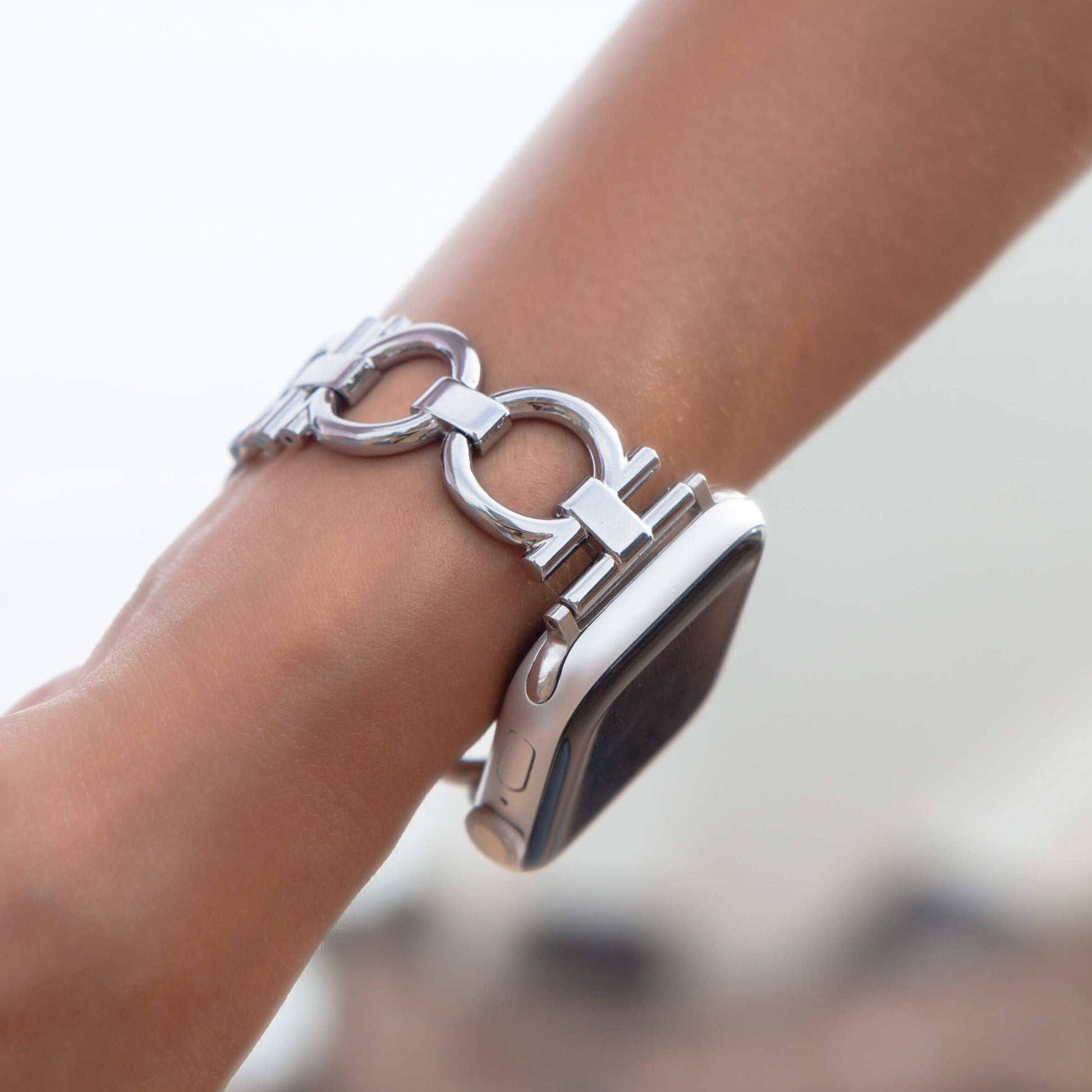Silver circle link Apple Watch band worn on a wrist against a bright sky. Slim metal iWatch strap, easily resizable with no tools, compatible with Apple Watch 38mm to 49mm, Series 1-11, SE and Ultra