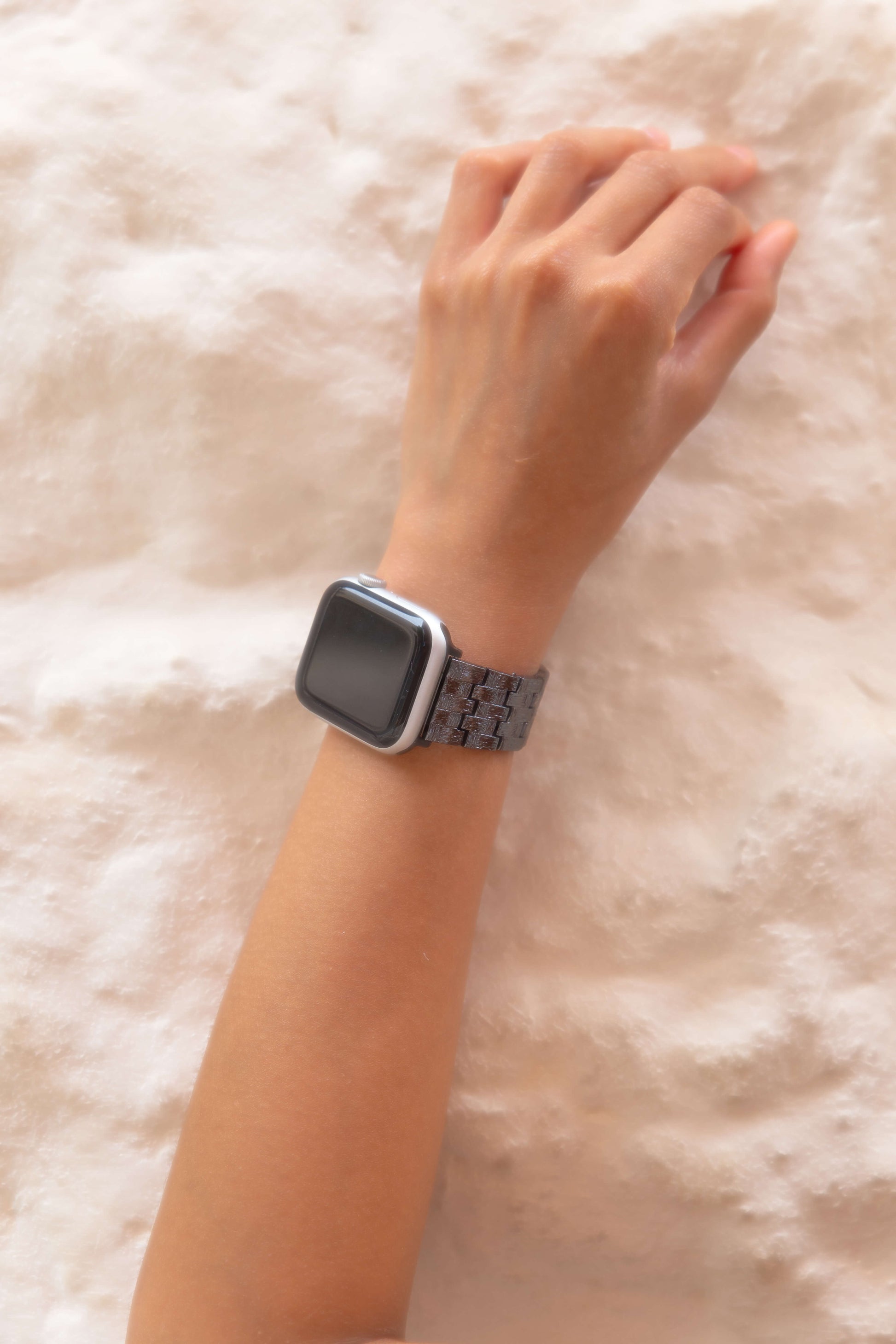 Black Baroque Apple Watch band worn on a wrist resting on soft white wall. Metal iWatch strap with brushed matte and polished shine, compatible with Apple Watch 38mm to 49mm, Series 1-11, SE and Ultra