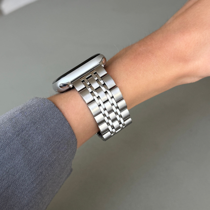 Silver link Apple Watch band worn on a wrist against a plain grey background. Unisex stainless steel metal armband, compatible with Apple Watch 38mm to 49mm, Series 1-11, SE and Ultra