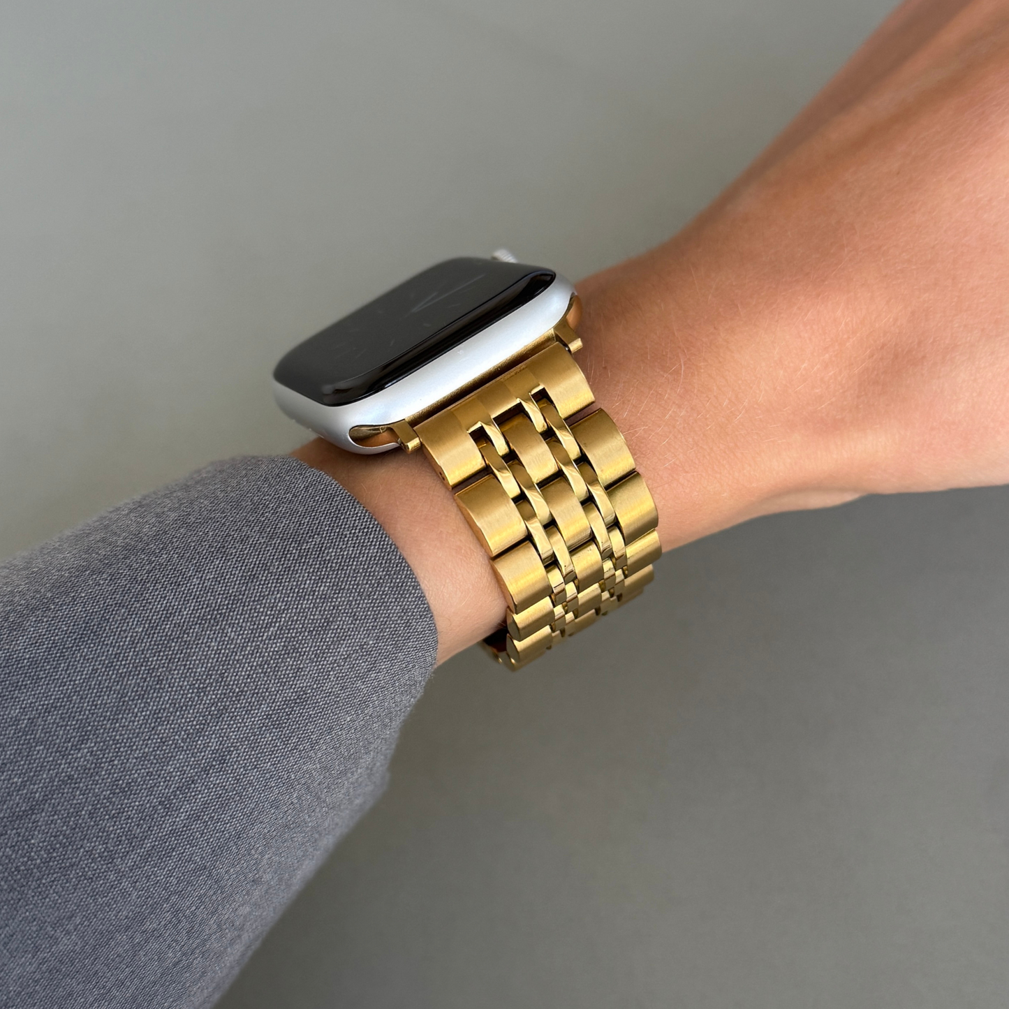 Gold link Apple Watch band worn on a wrist with a grey sleeve. Waterproof stainless steel metal armband, compatible with Apple Watch 38mm to 49mm, Series 1-11, SE and Ultra
