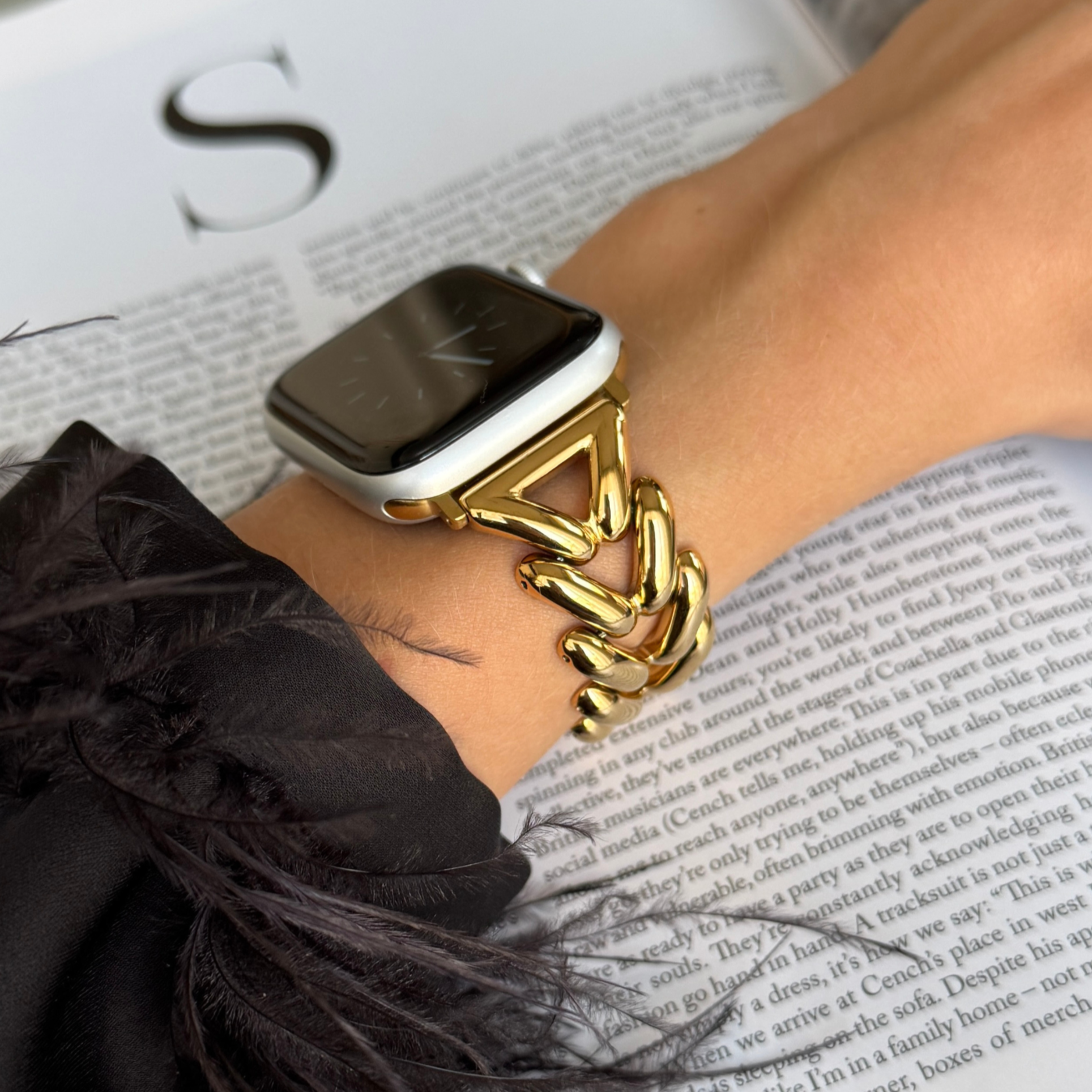 Gold chunky chain Apple Watch band worn on a wrist with a feather trimmed sleeve. Luxury metal iWatch bracelet for women, compatible with Apple Watch 38mm to 49mm, Series 1-11, SE and Ultra