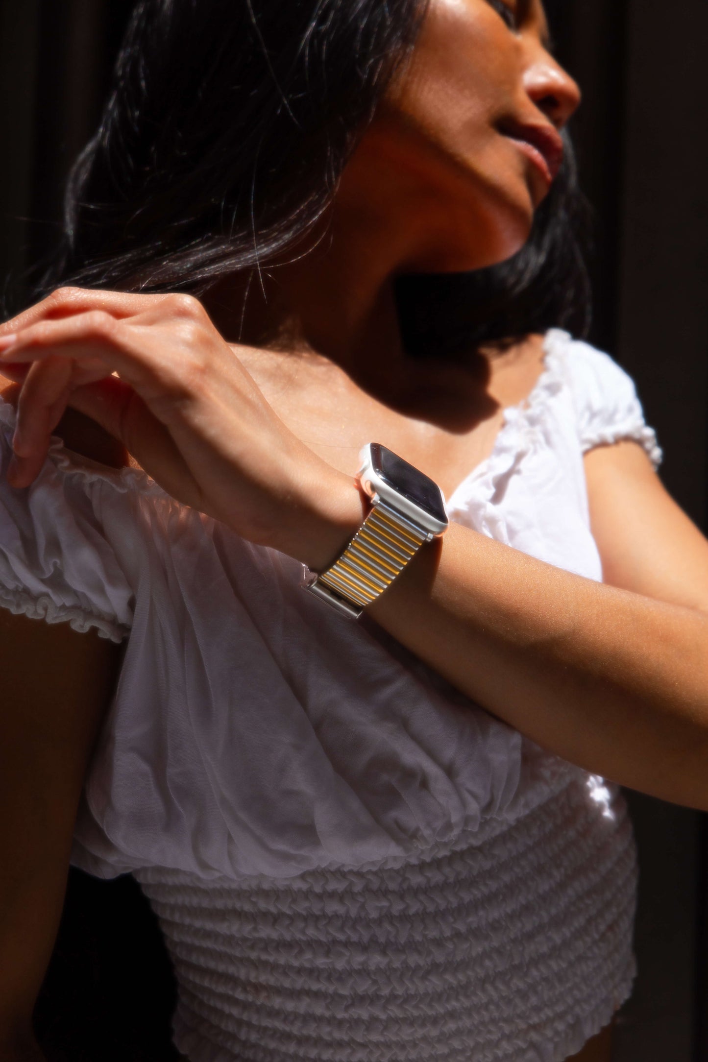 Silver gold ribbed loop Apple Watch band worn by a woman in a white top. Chic stainless steel iWatch strap, compatible with Apple Watch 38mm to 49mm, Series 1-11, SE and Ultra