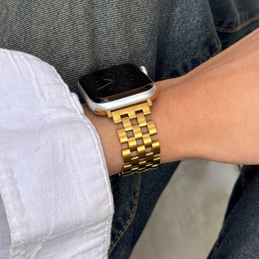 Gold multi link Apple Watch band worn on a wrist with a white shirt over denim. Minimalist brushed matte stainless steel iWatch bracelet, compatible with Apple Watch 38mm, 40mm, 41mm, 42mm, 44mm, 45mm, 46mm and 49mm, Series 1-11, SE and Ultra