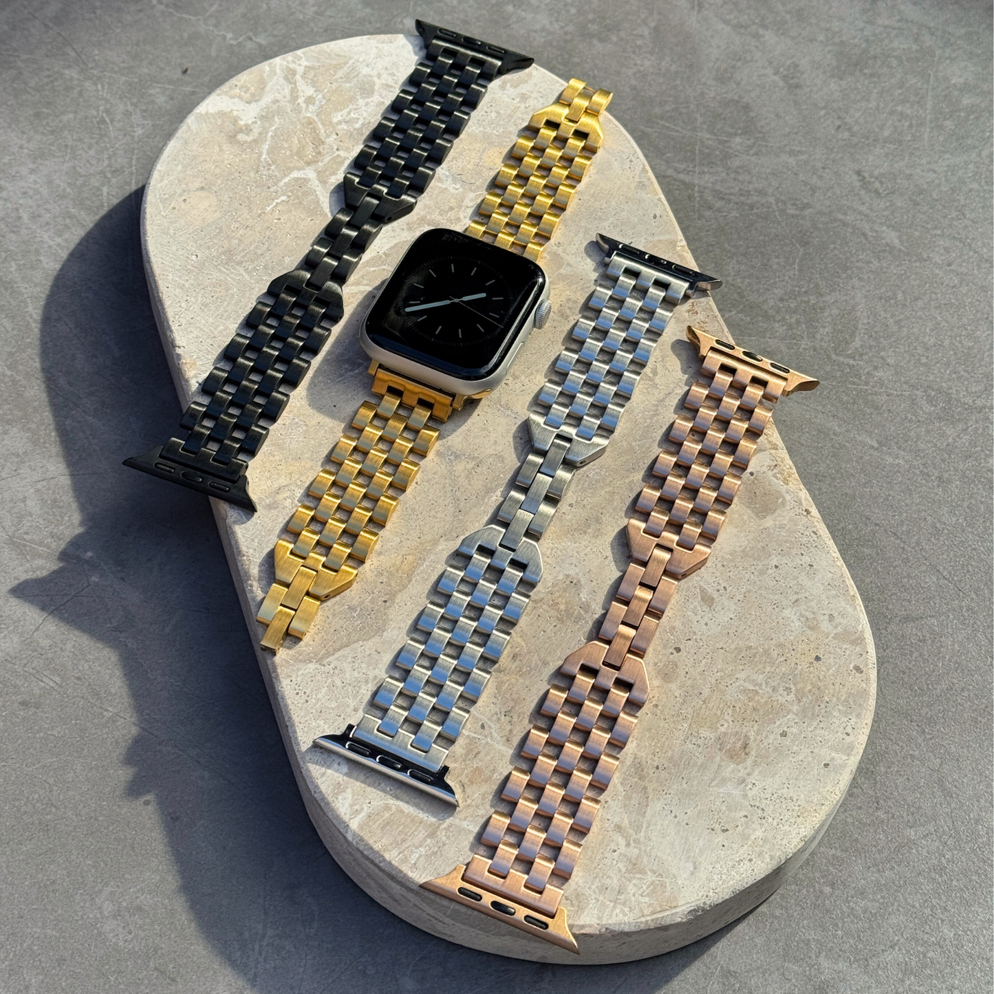 Black, gold, silver and rose gold multi link Apple Watch bands laid out on a stone tray. Premium brushed matte stainless steel iWatch straps, compatible with Apple Watch 38mm to 49mm, Series 1-11, SE and Ultra