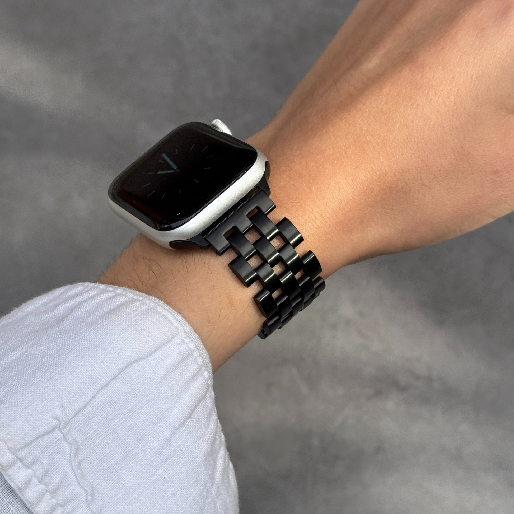 Black multi link Apple Watch band worn on a wrist against a grey background. Minimalist stainless steel iWatch bracelet with an architectural edge, compatible with Apple Watch 38mm to 49mm, Series 1-11, SE and Ultra
