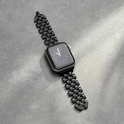 Black multi link Apple Watch band lying flat on grey concrete. Modern stainless steel iWatch strap with a seamless link profile, compatible with Apple Watch 38mm to 49mm, Series 1-11, SE and Ultra