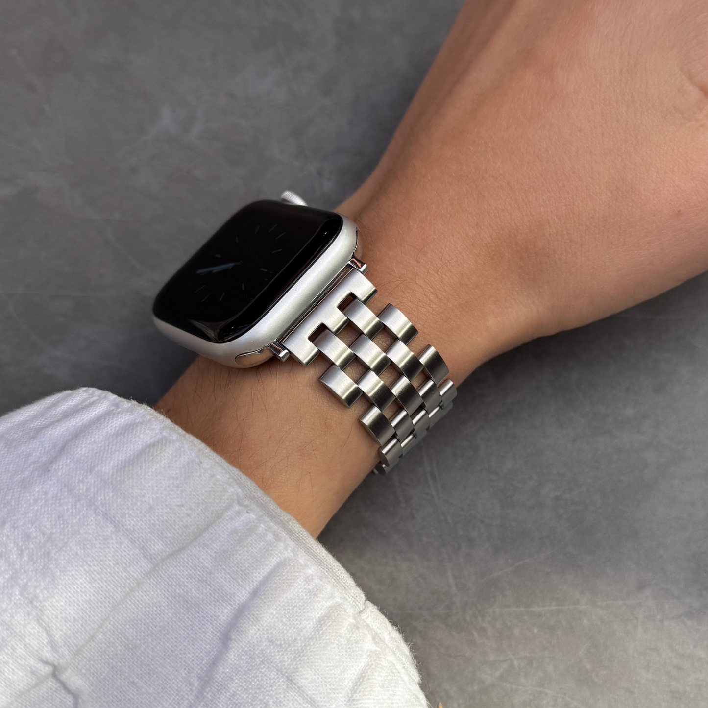 Silver multi link Apple Watch band worn on a wrist with a white linen sleeve. Unisex brushed matte stainless steel iWatch bracelet, compatible with Apple Watch 38mm to 49mm, Series 1-11, SE and Ultra
