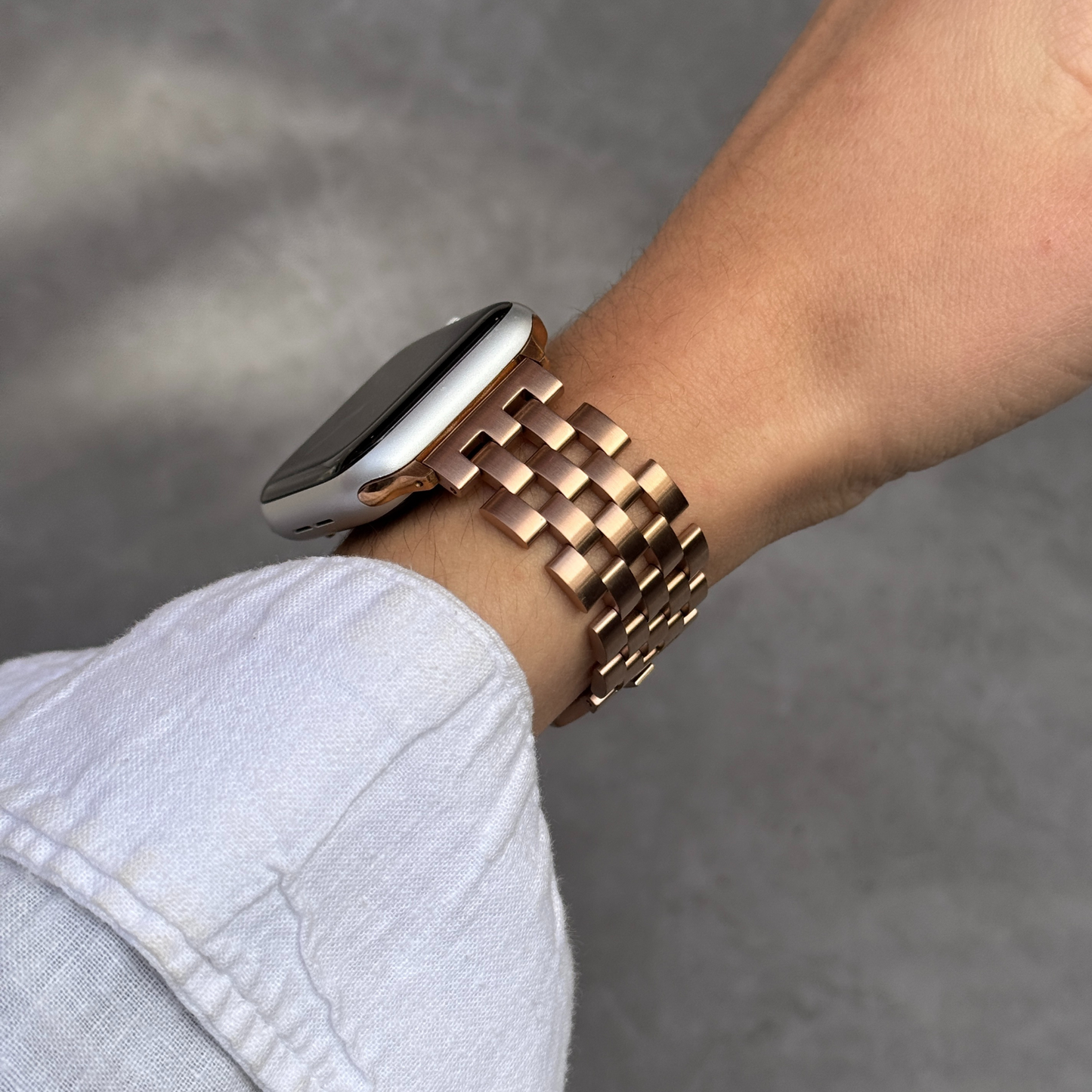 Rose gold multi link Apple Watch band worn on a wrist with a pale sleeve. Minimalist stainless steel iWatch bracelet with understated sophistication, compatible with Apple Watch 38mm to 49mm, Series 1-11, SE and Ultra