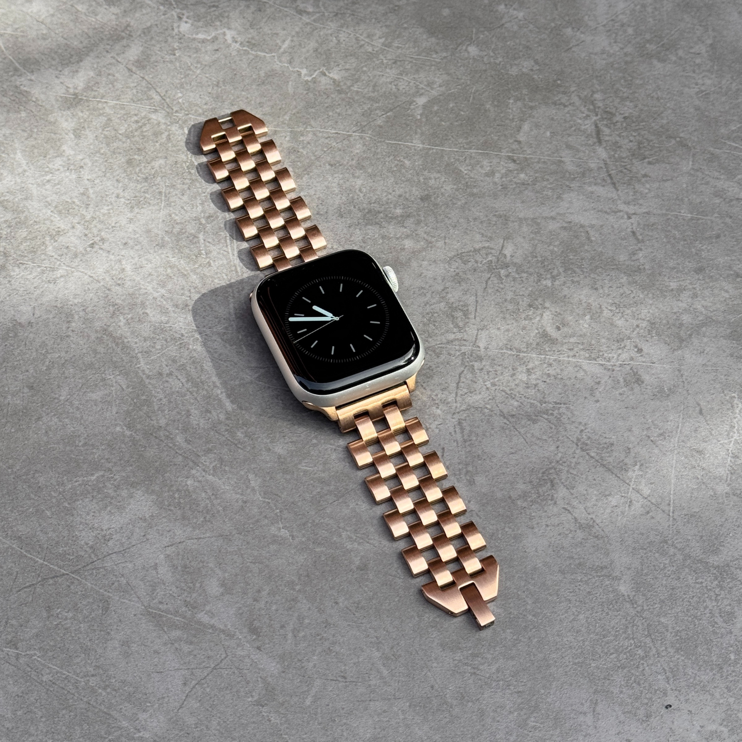 Rose gold multi link Apple Watch band lying flat on grey concrete. Modern brushed matte stainless steel iWatch strap, compatible with Apple Watch 38mm to 49mm, Series 1-11, SE and Ultra